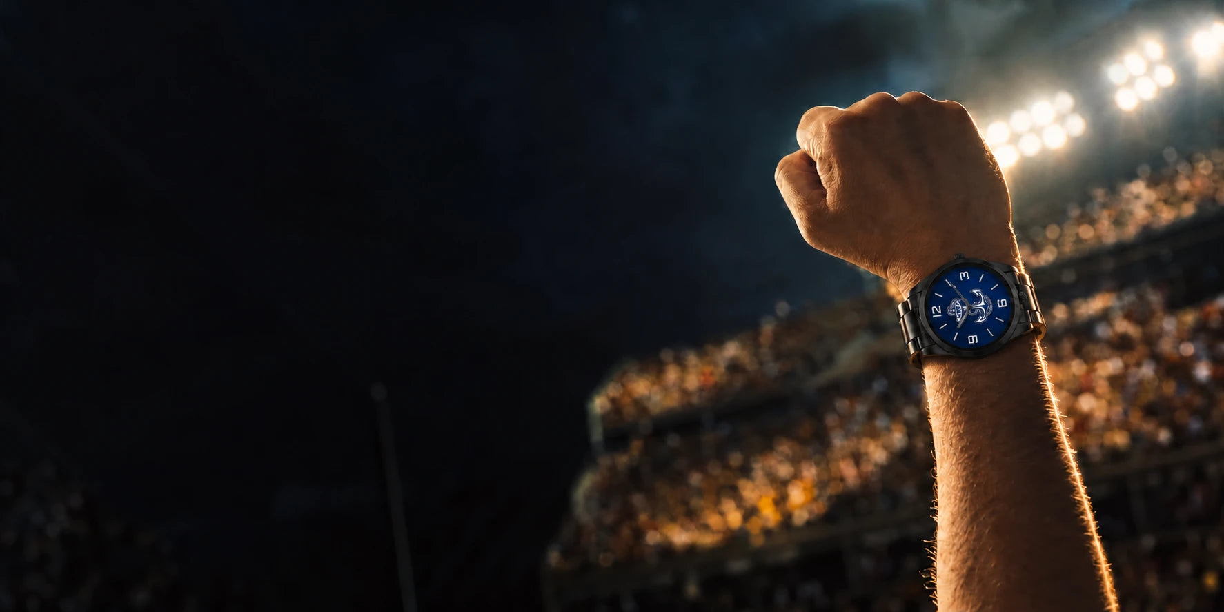 Raised fist and wrist wearing a LicensedTime team watch at a college football game at dusk